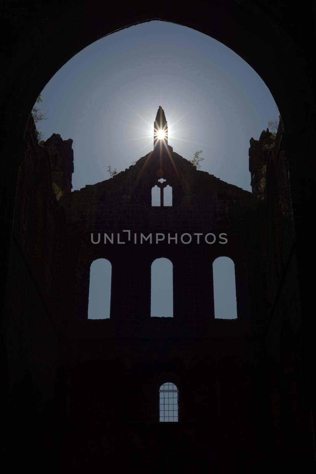 Plants grow atop the stone walls of this ruined cathedral, and sun flare enhances religious feeling of this ruined cathedral. Old windows silhouetted