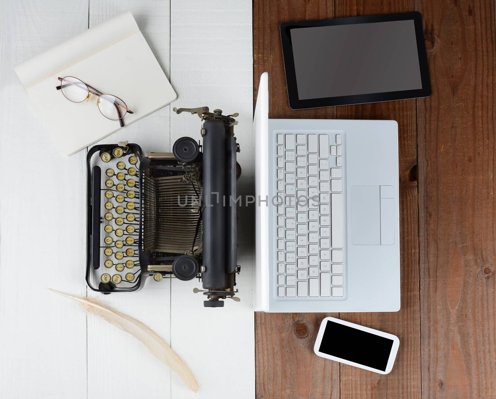 Overhead shot of and old fashioned desk with typewriter and quill pen back-to-back with a modern set up with laptop computer, tablet and cell phone, (Phone and Tablet created in Photoshop - not real)
