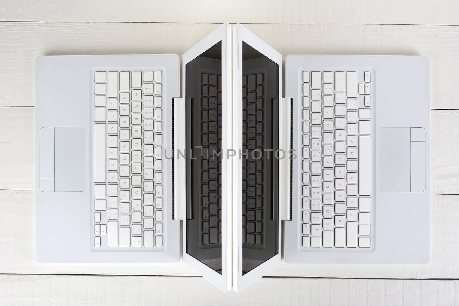 High angle shot of two white laptop computers back-to-back on a white wood table. Horizontal format.