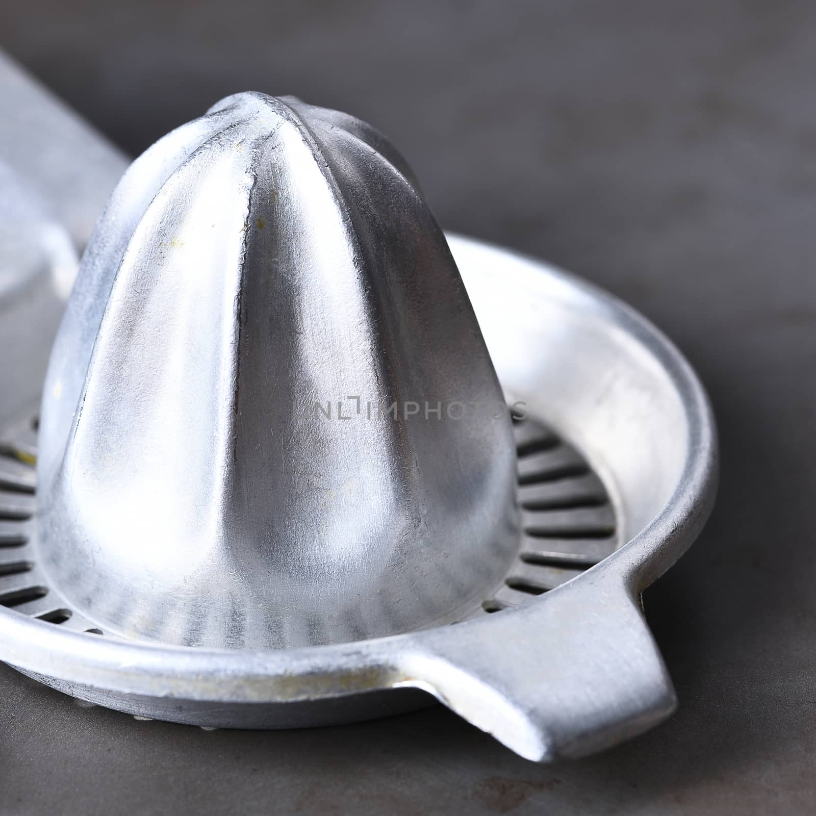 Closeup of an antique juicer. The shiny metal kitchen implement is on a gray metal surface.