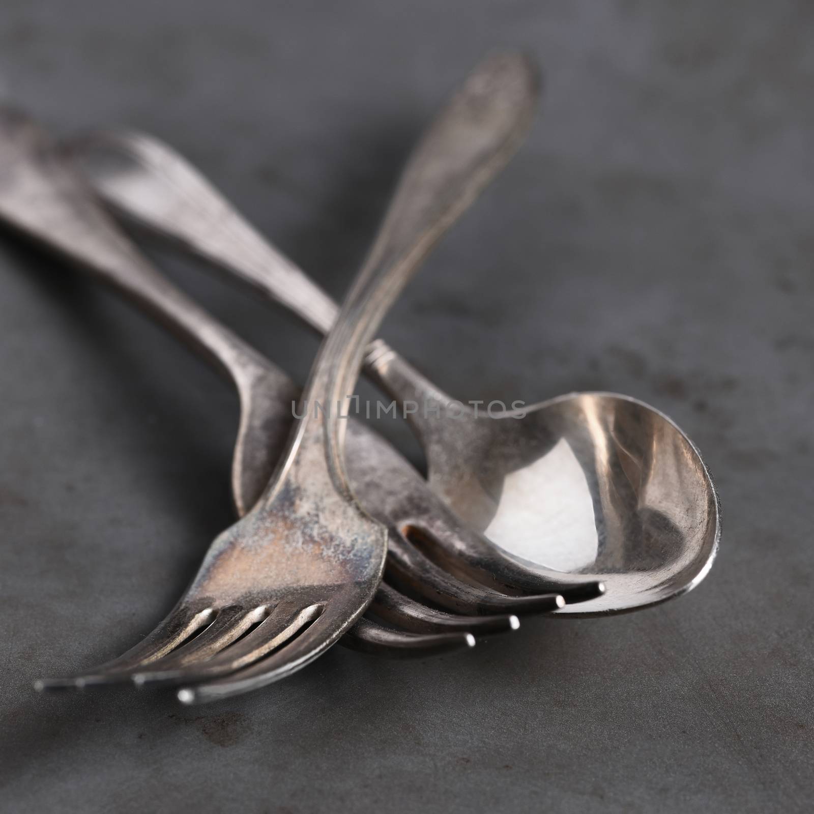 Closeup still life of antique forks and spoon on gray metal background,. Shallow depth of field. 
Square format.