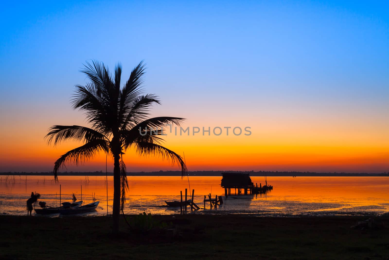 A silhouette of hut with background beautiful of sunset colorful sky reflect on water in dam location at north east of Thailand