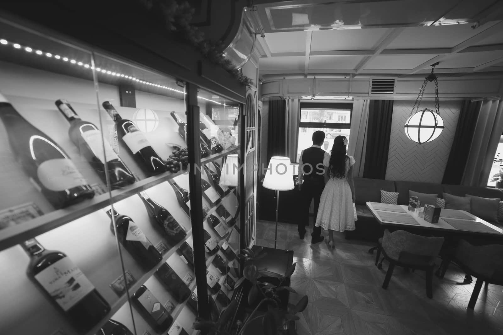 The bride and groom are in the restaurant. They're looking out the window. Wine bottles. Wedding by selinsmo