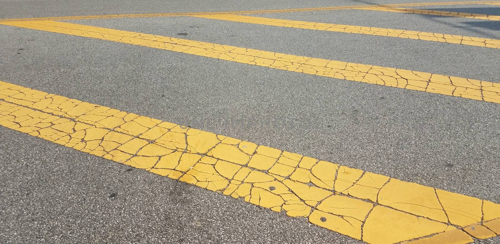 worn or weathered yellow lines with cracks on black asphalt