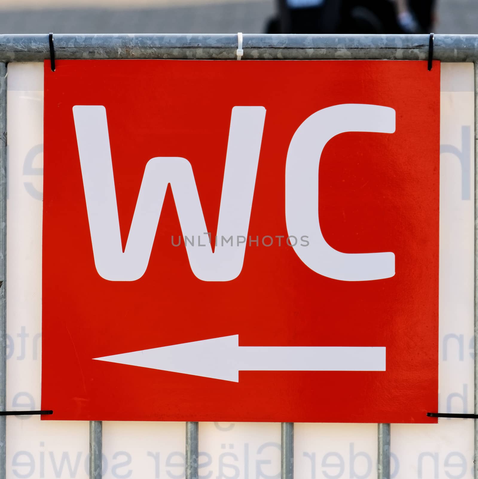 Red sign on the outdoor area at a festival with the white written sign "WC" and an arrow pointing towards the toilet by geogif