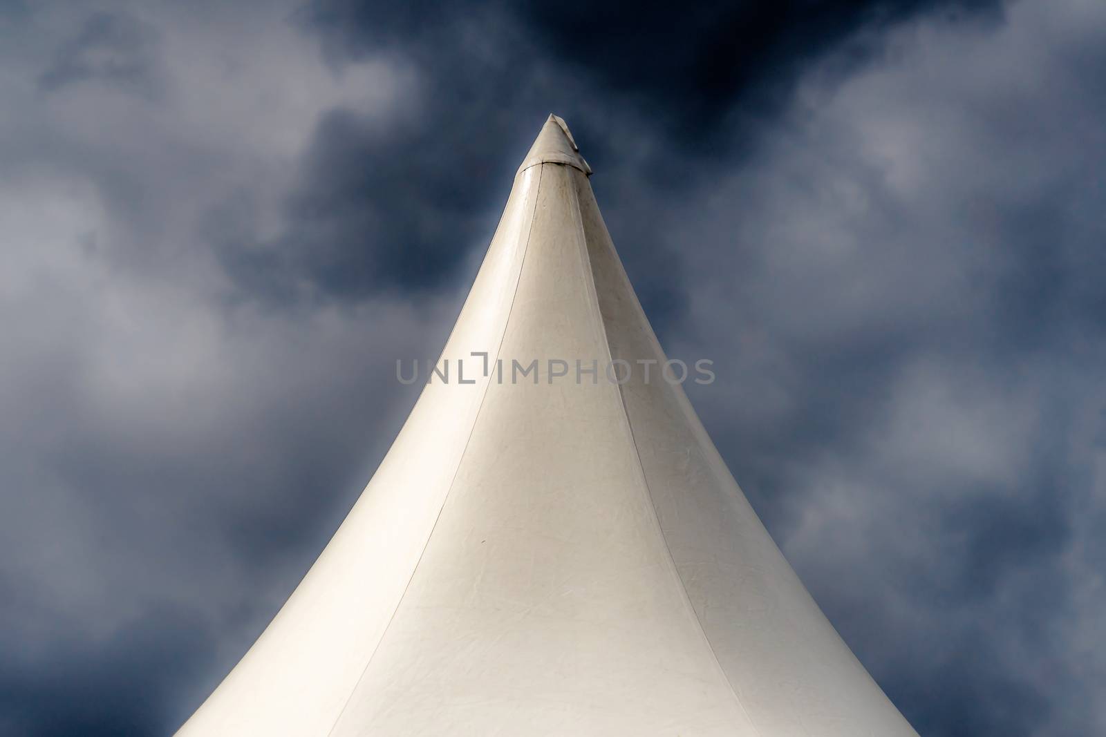 Abstract artistic shot from the top of a white tent in front of a threatening dramatic grey sky with clouds by geogif