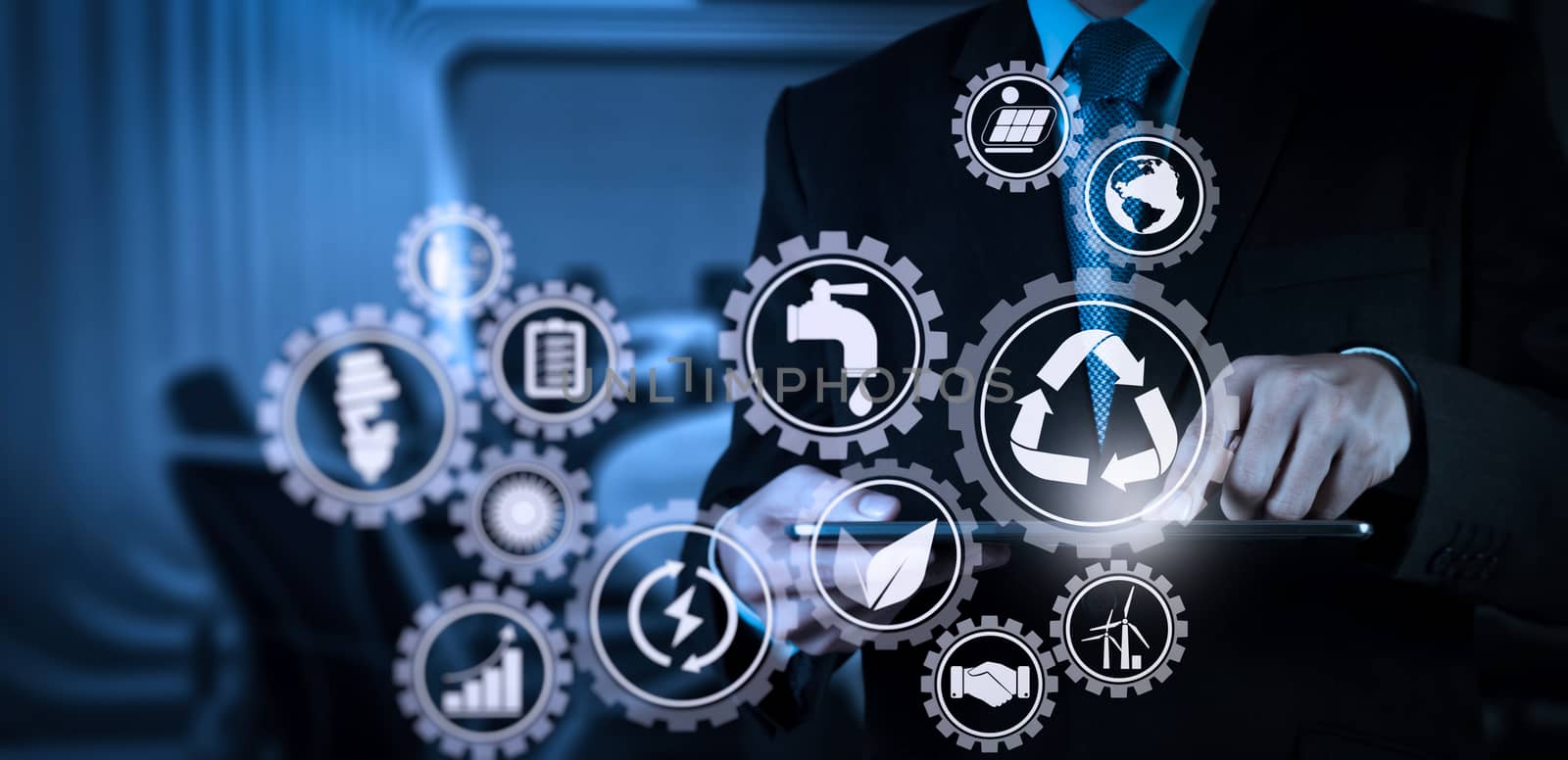 Sustainable development with icons of renewable energy and natural resources preservation with environment protection inside connected gears.Businessman hand working with a digital tablet on meeting room background