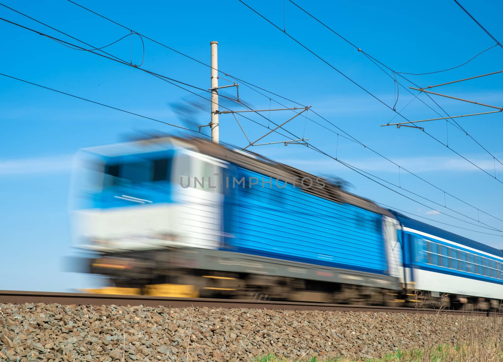 Blue train powered by electricity, drives through the countryside.