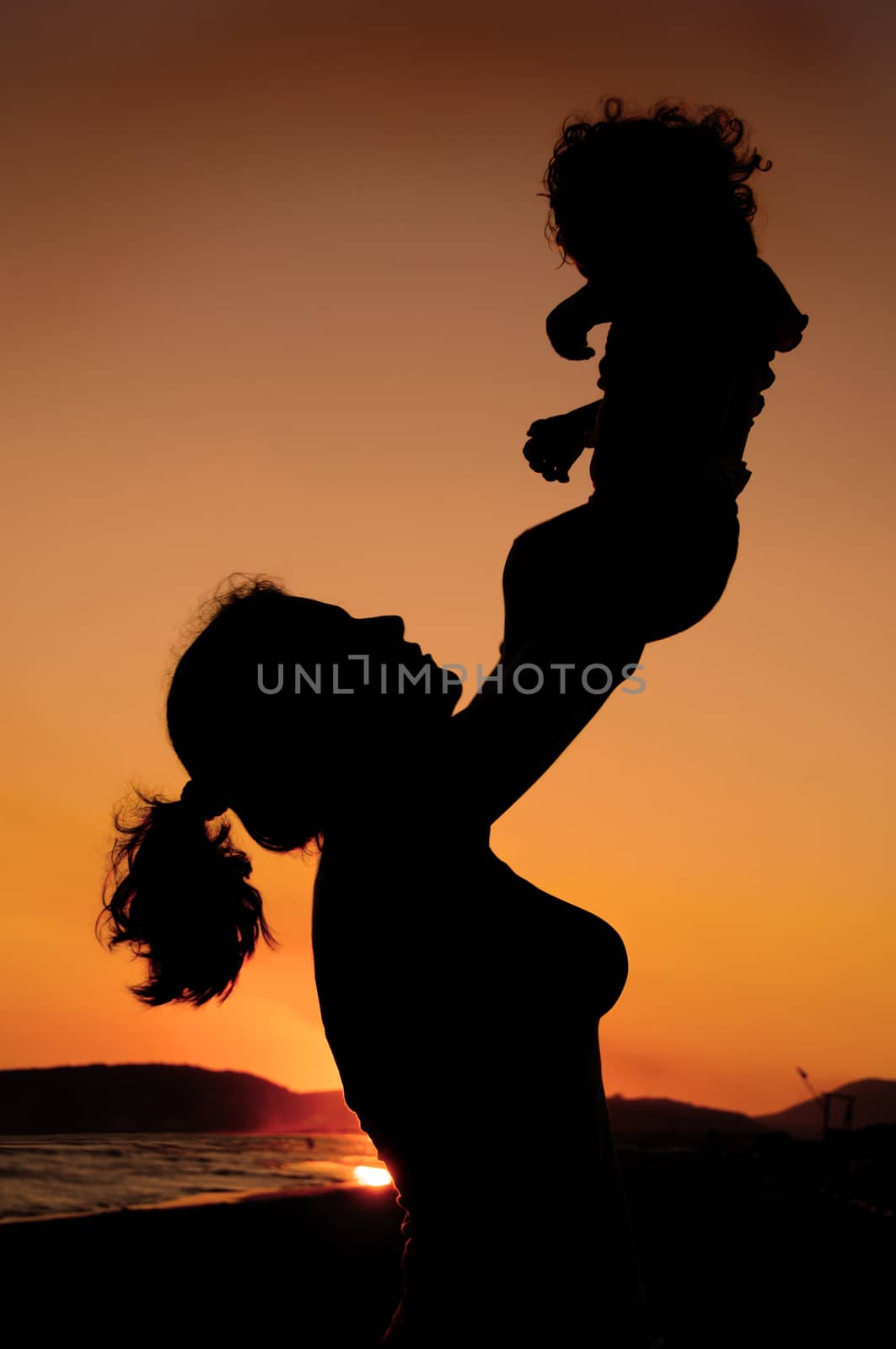 Silhouette of mother and child on the beach 
 on beautiful summer sunset 