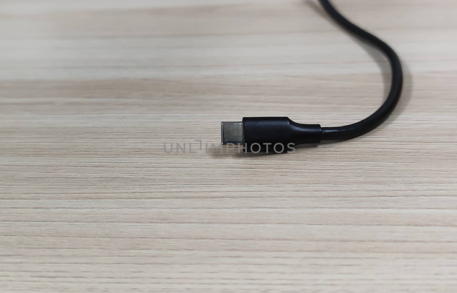 Close-up of a black type-c charging cable on a wooden table background.