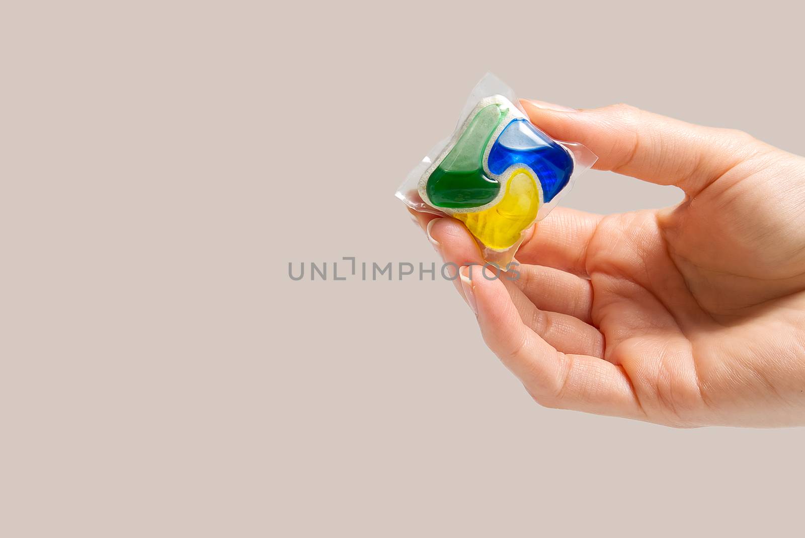 hand holds the Dishwasher Capsule on beige background. copy space, woman hand holding dishwasher detergent tablet.