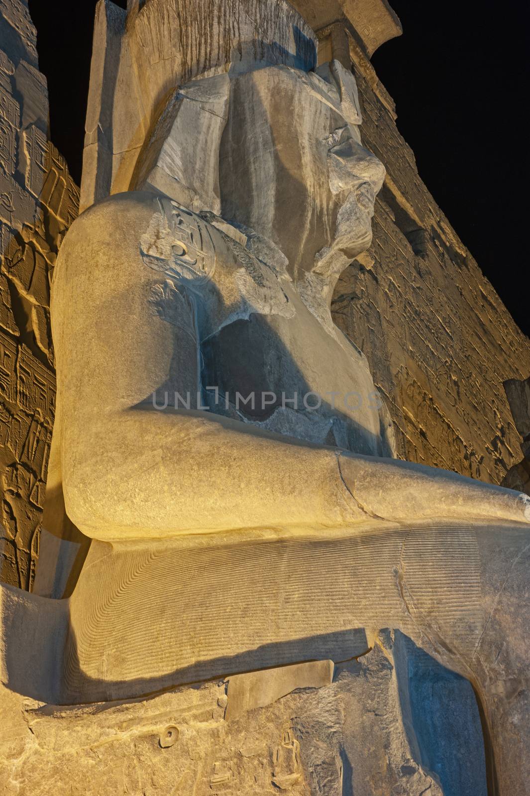 Large statue of Ramses II at entrance pylon to ancient egyptian Luxor Temple lit up during night