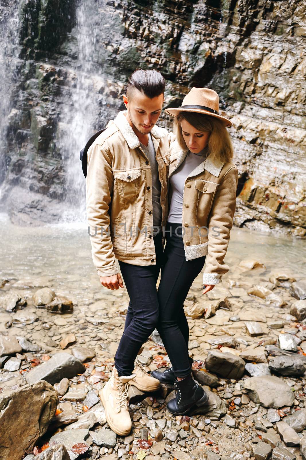 Young and beautiful couple at the mountain waterfall - Happy tourists visiting mountains. Lovestory. Tourists in hats. Military fashion