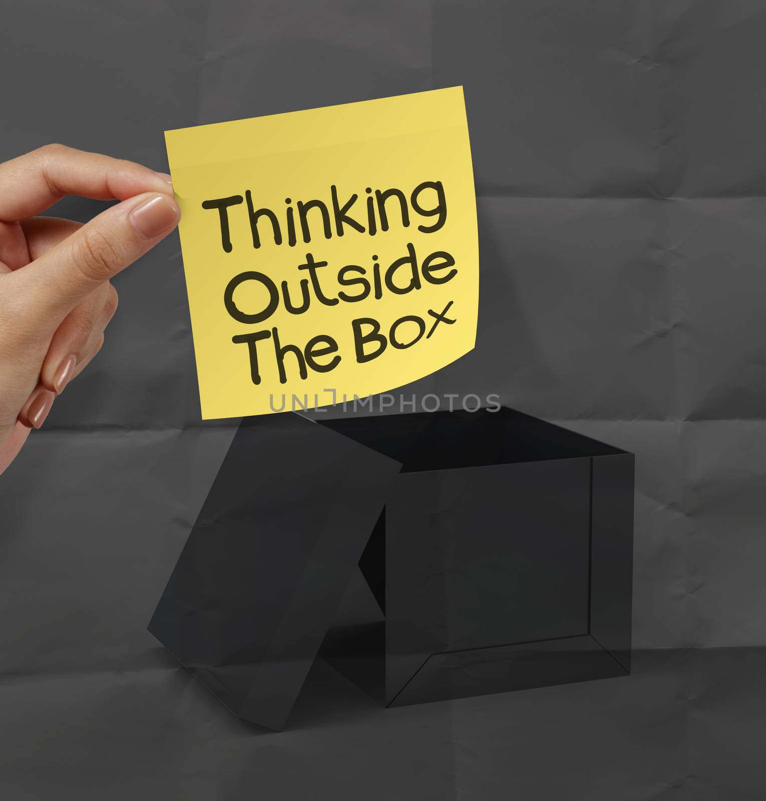 hand holding sticky note with thinking outside the box on dark crumpled paper as concept
