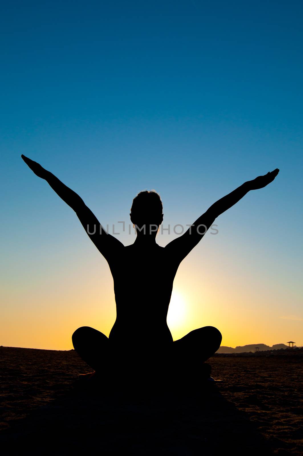 Silhouette of woman in yoga lotus meditation position with arms up