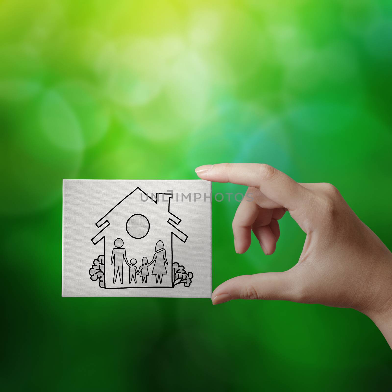 hand showing hand drawn house with family icon on canvas board on green nature background as insurance concept 
