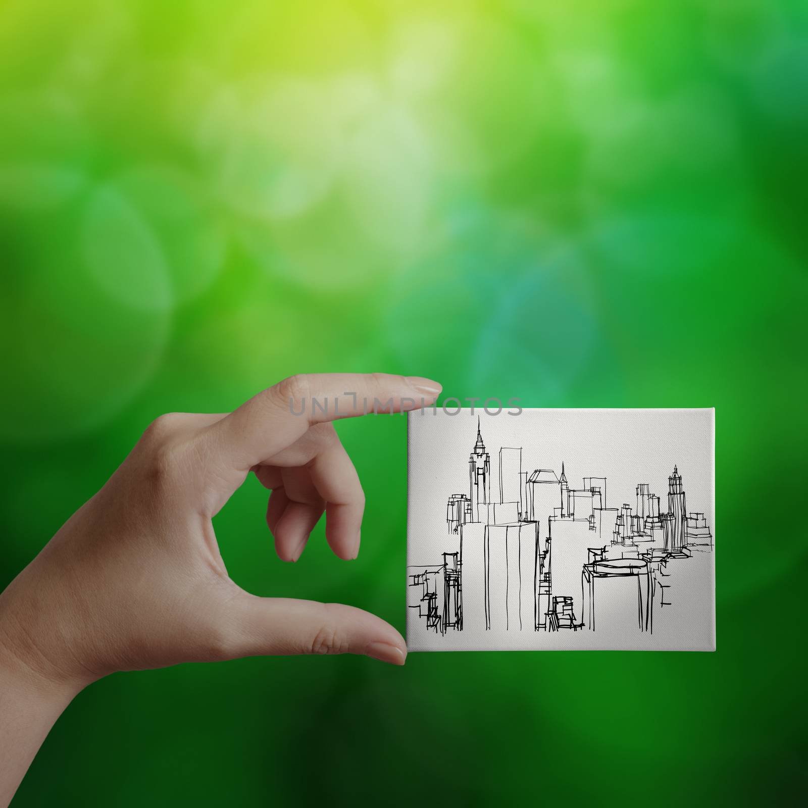 hand showing hand drawn city on canvas board on green nature background as concept