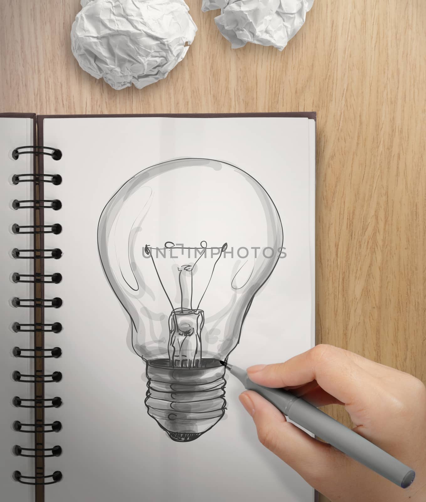 hand with a pen drawing light bulb on note book as concept by everythingpossible