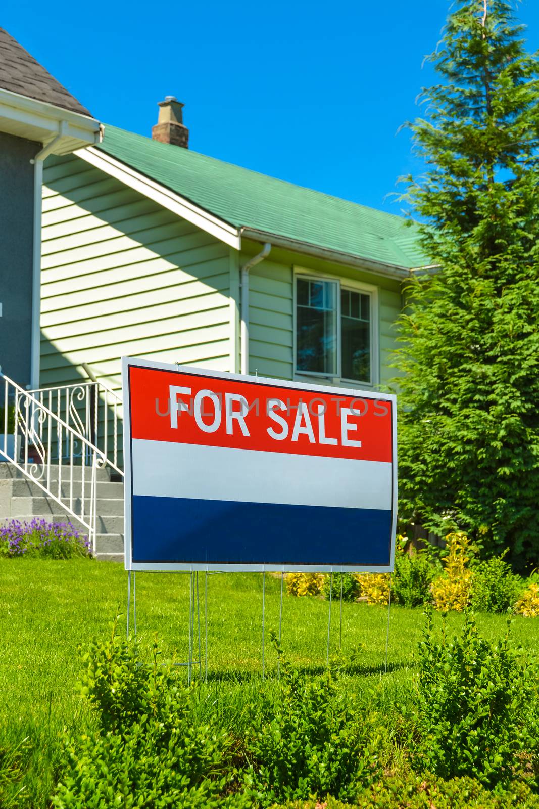 Real estate sign 'For Sale' on front yard of a house.