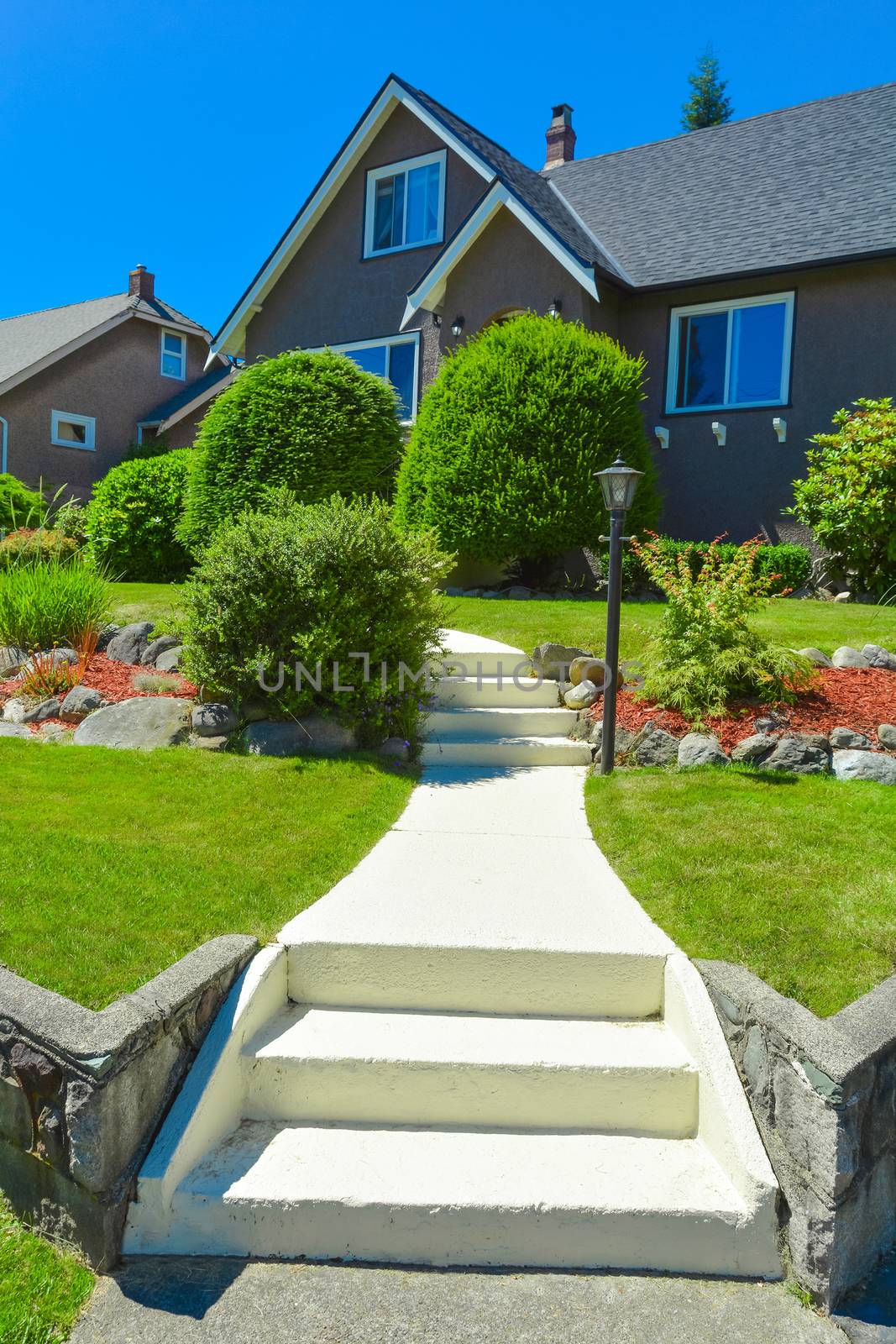 Concrete pathway with steps leading to residential house. Front yard of family house with landscaping on blue sky background