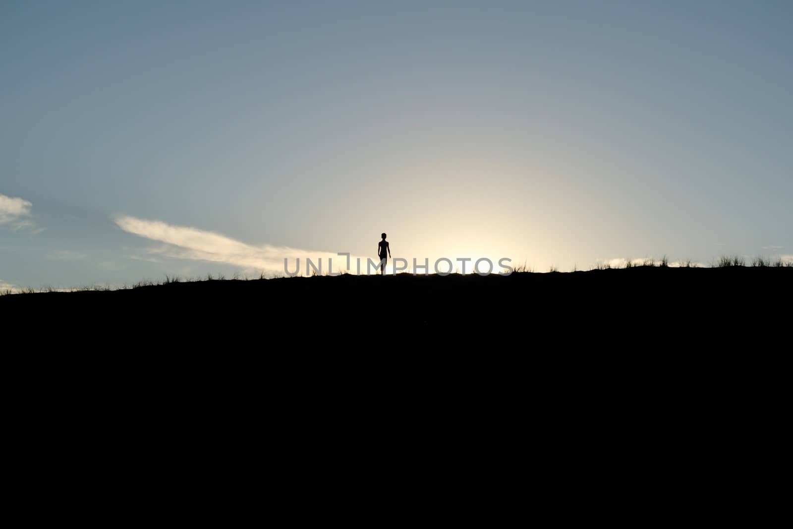 Young boy silhouetted against the sun atop a dune in the desert