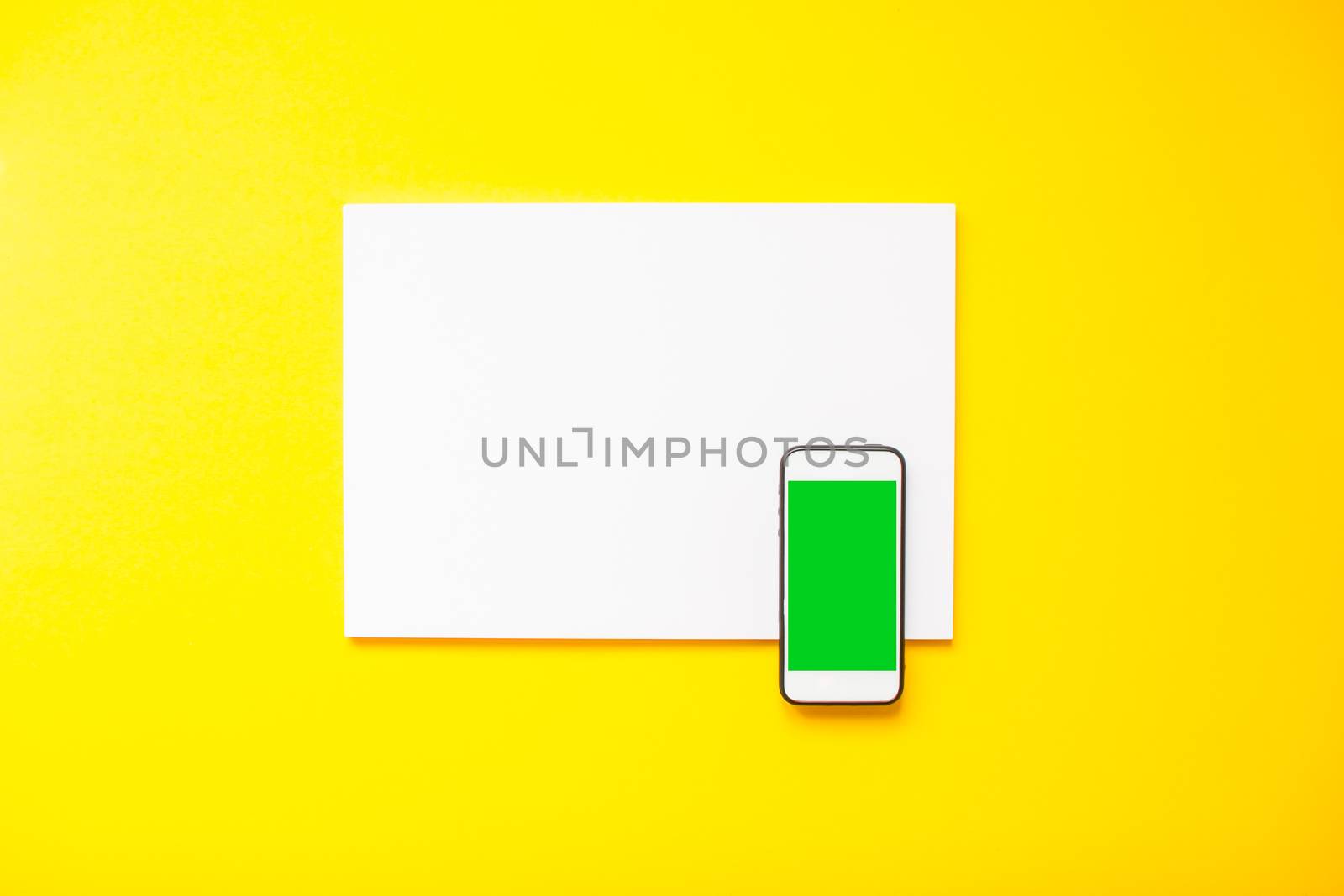 blank white sheet and smartphone on a bright yellow background. by malyshkamju