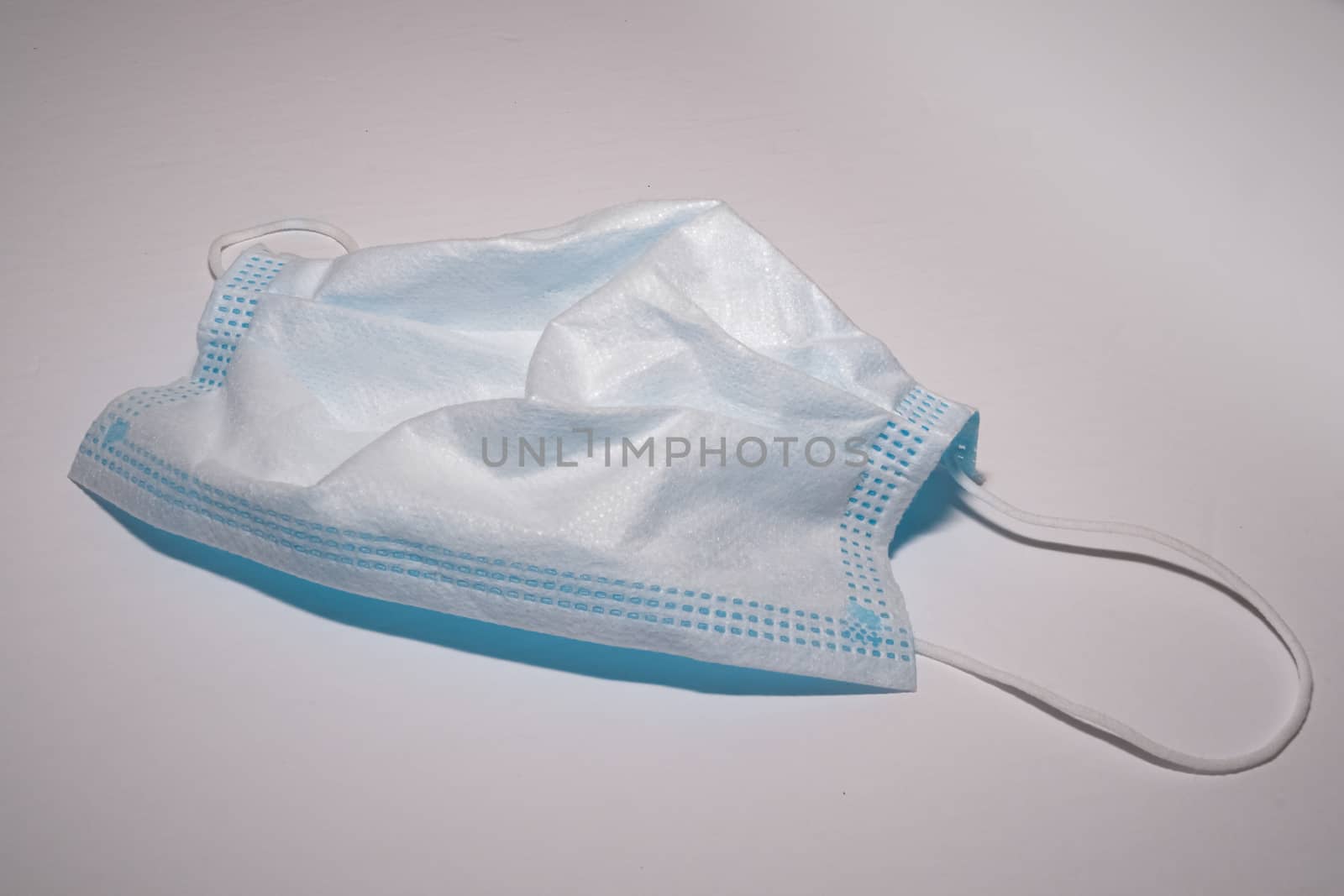 A single, white, hospital-grade medical face mask is laid out on a white surface.