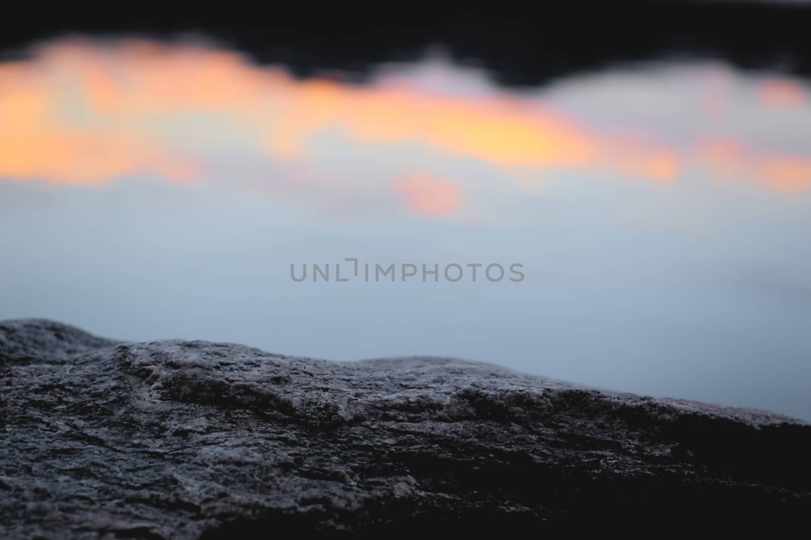 Calm, serene natural environment. Rock texture close up against twilight sky reflections on a lake.