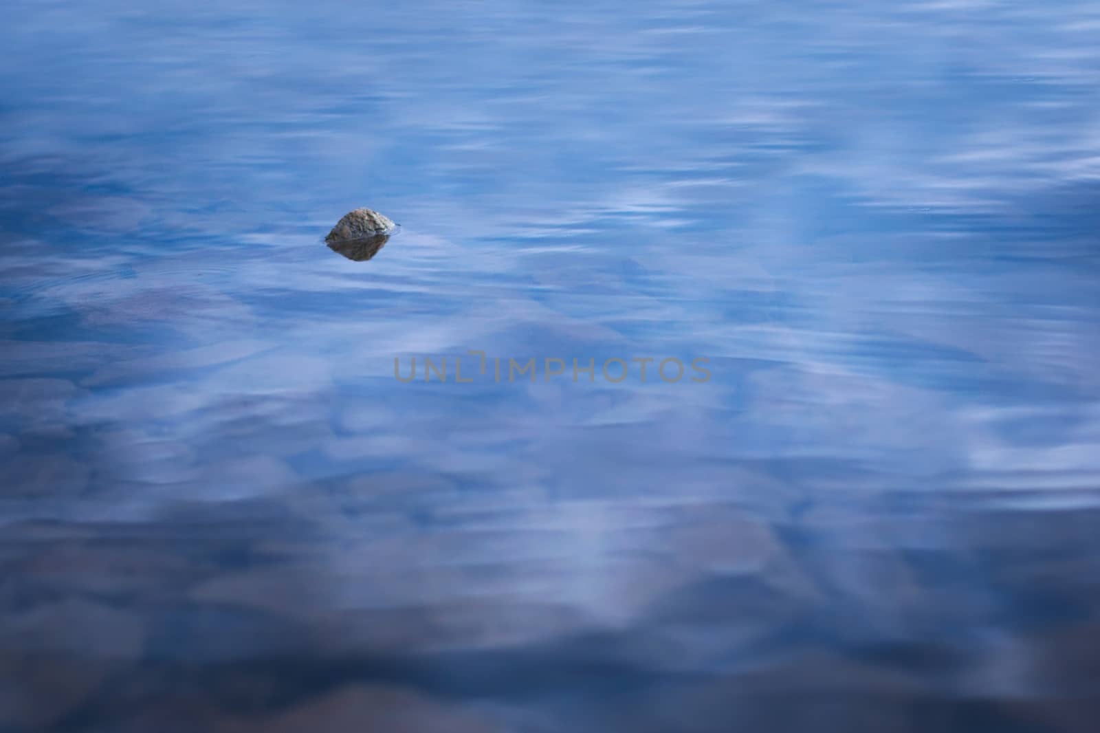 Single stone on shallow waters of a lake at dusk by hernan_hyper