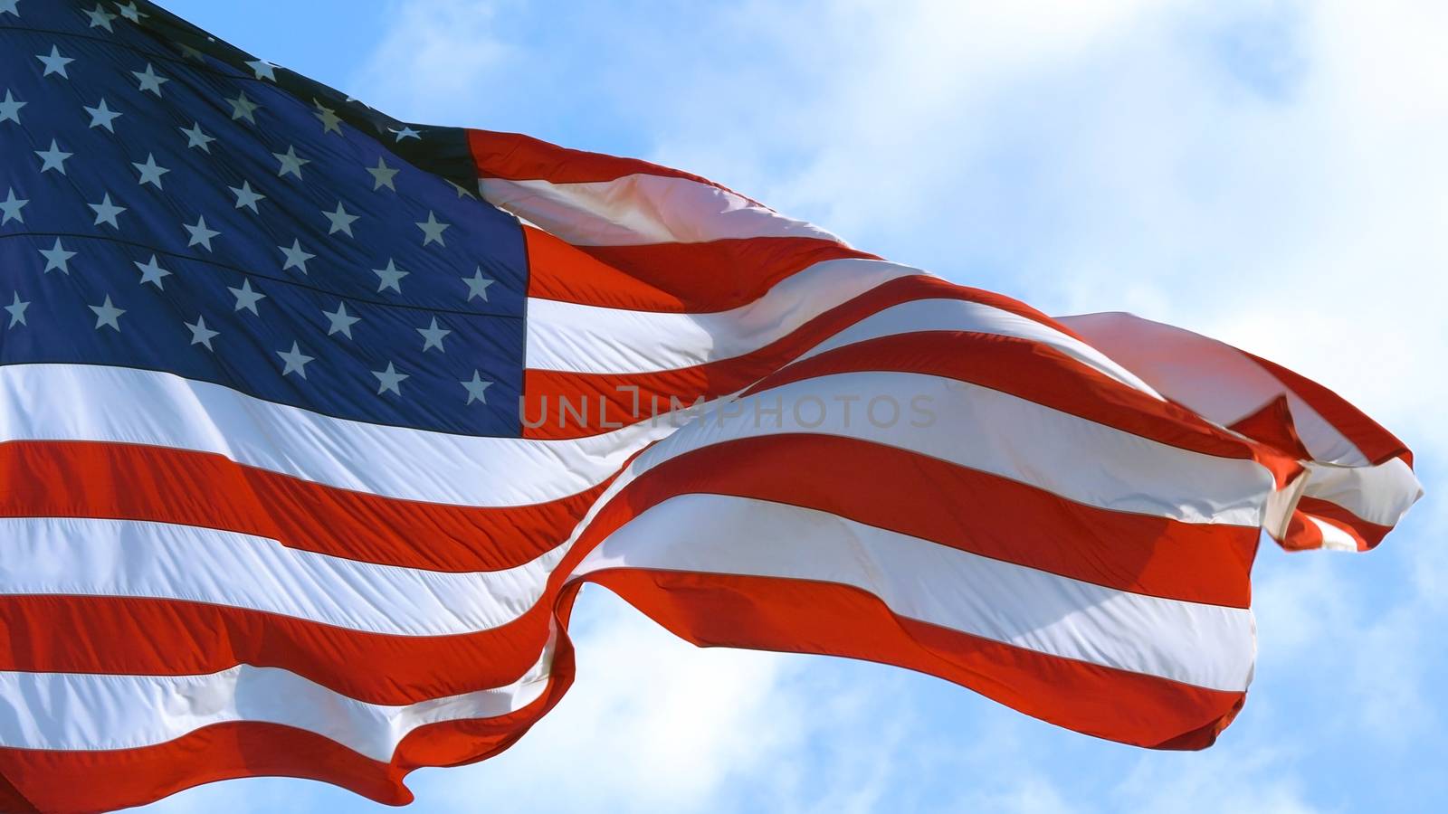 American Flag blowing in the wind with a blue sky background. USA American Flag. Waving United states of America famous flag in front of blue sky. Independence Day. Elections Day