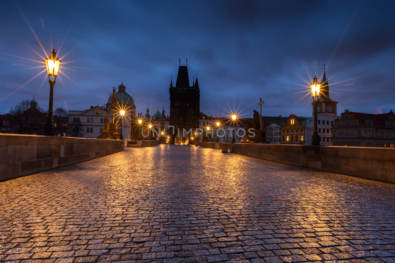 Historic bridge in Prague at sunrise with lights reflecting on the wet stone