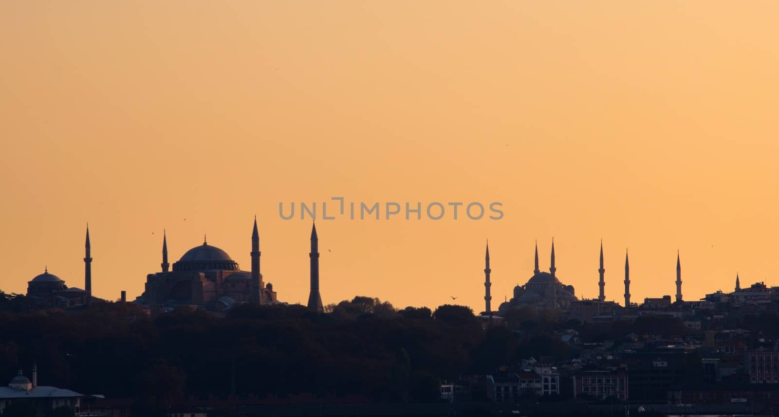 Silhouette of Hagia Sophia and the Blue Mosque of Sultanahmet, in Istambul, Turkey, against the ochre afternoon sky.