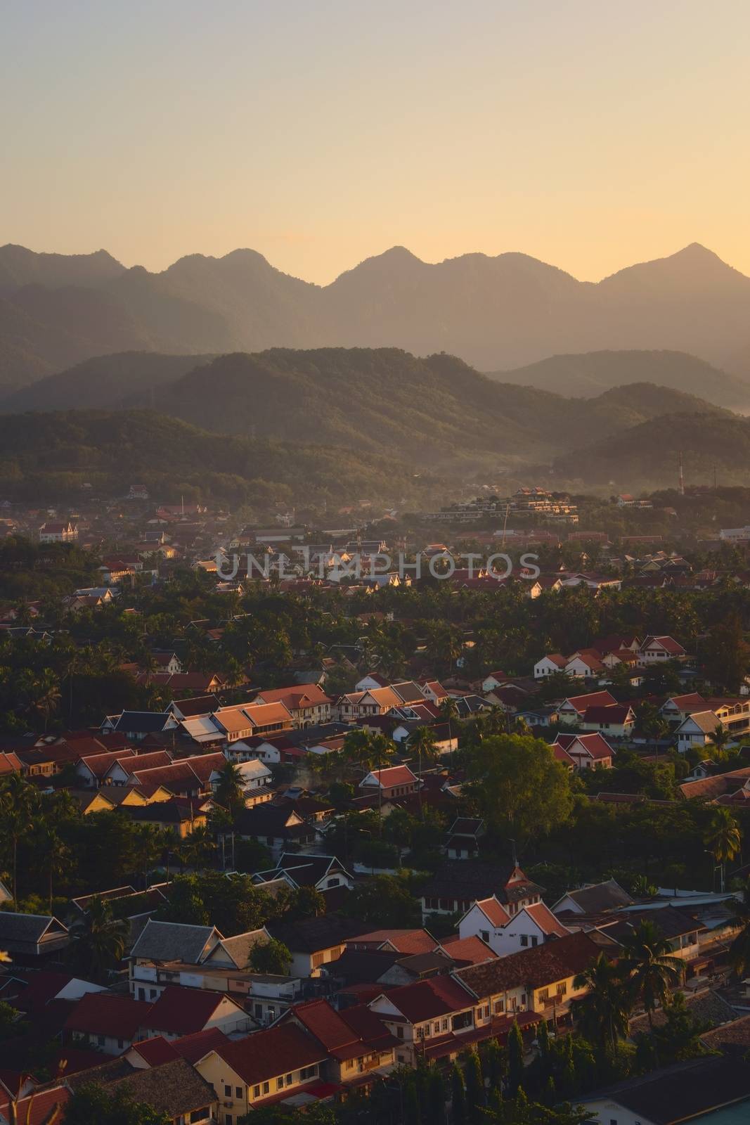 Elevated view of the city of Luang Prabang, Laos, at sunset, with mountains on the background. by hernan_hyper