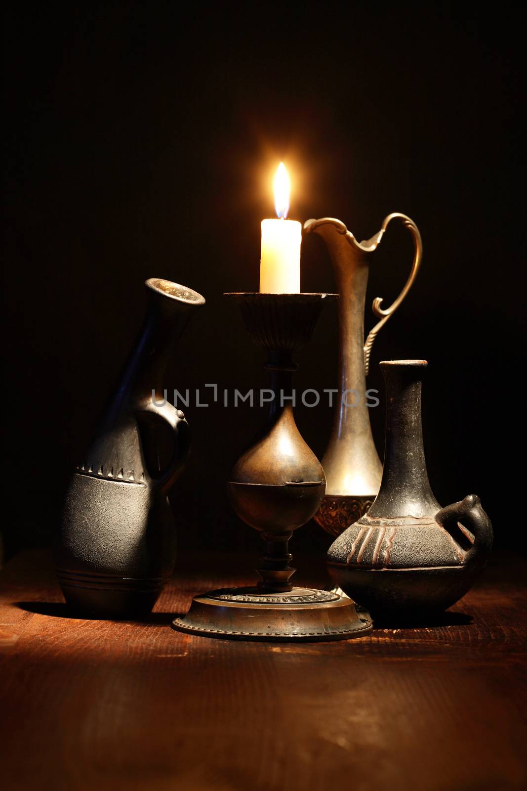 Set of nice ancient vases near lighting candle on dark background