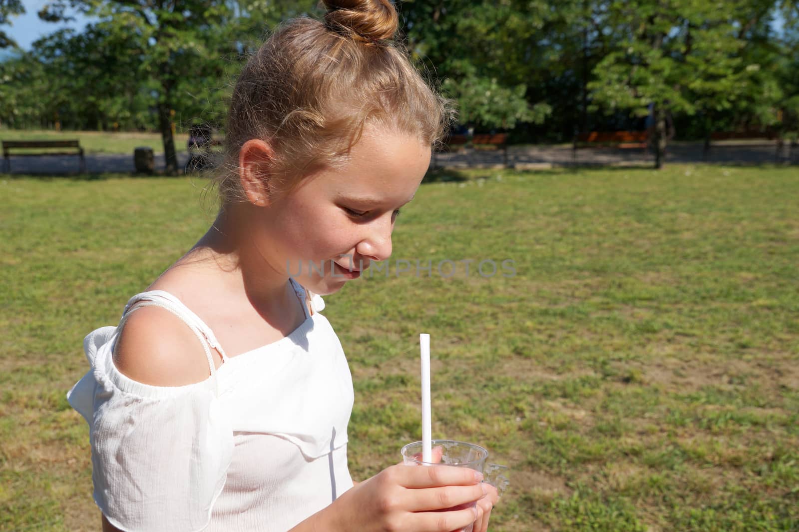 girl drinks fruit juice through a straw in summer park.