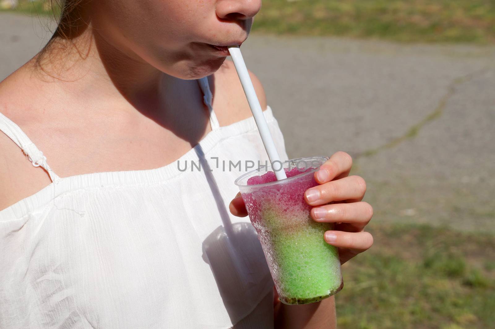 girl drinks fruit cocktail through a straw in a park on a sunny day by Annado