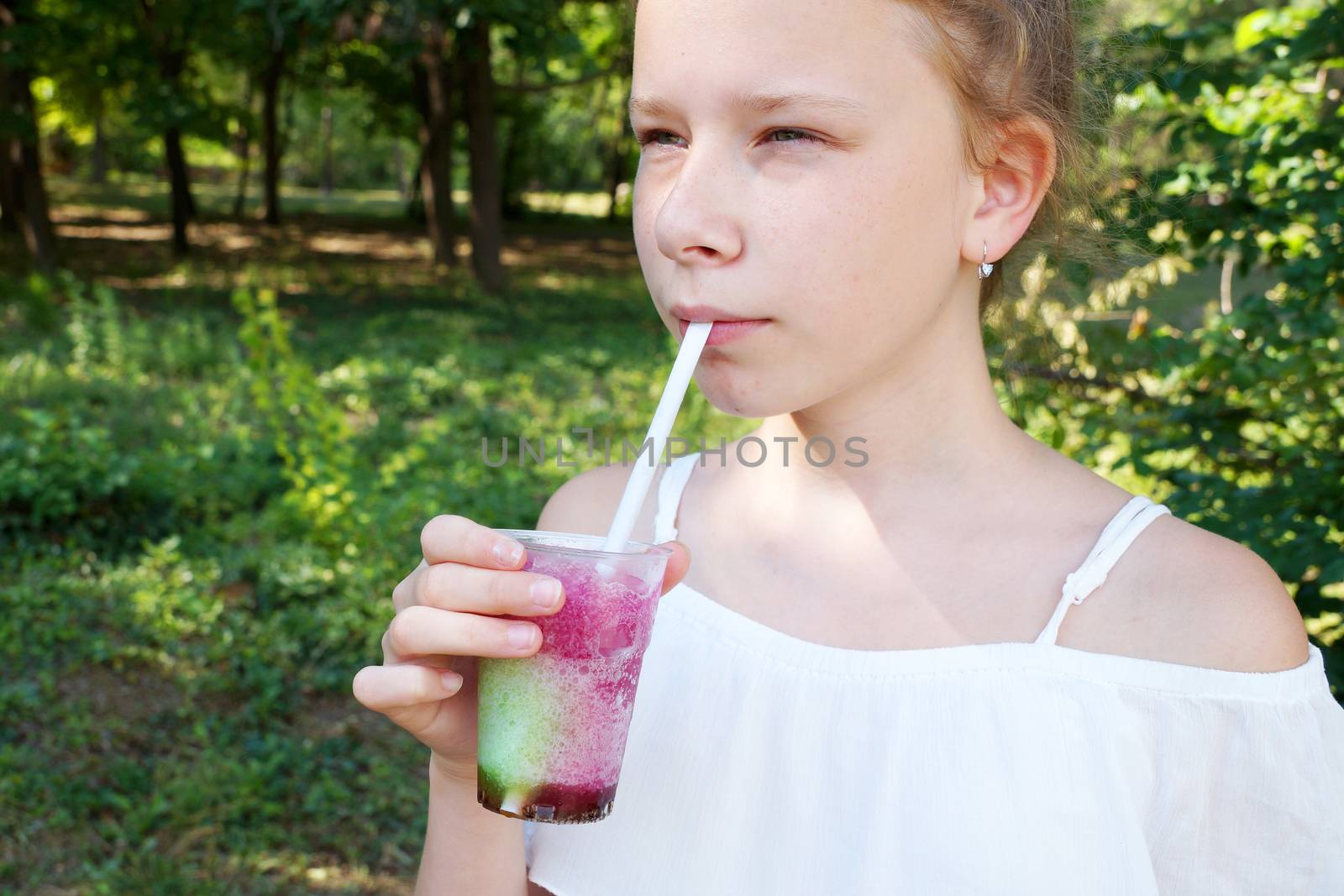 refreshing fruit drink with a straw in the hands of a girl in the park.