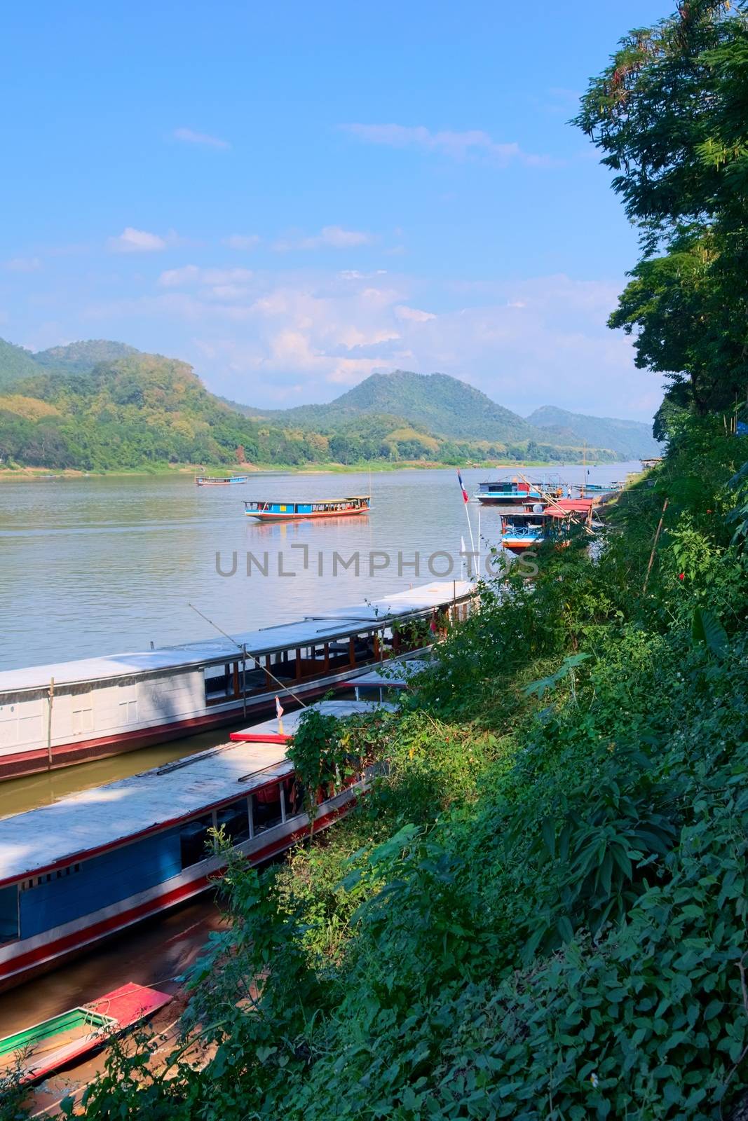 Long boats and barges sailing on the Mekong River near Luang Prabang, Laos. by hernan_hyper