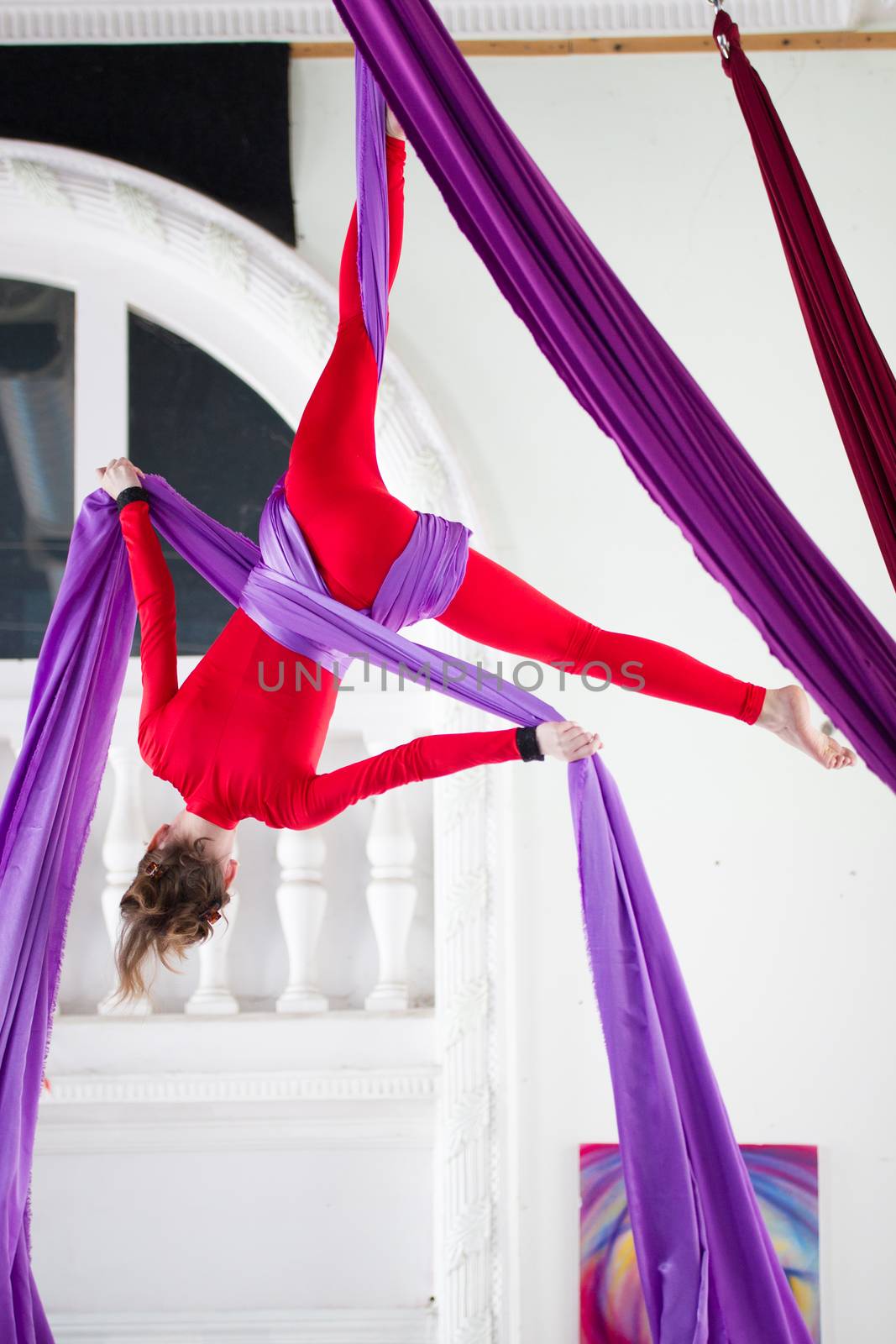Young attractive woman hangs upside down on the aerial silk, telephoto shot