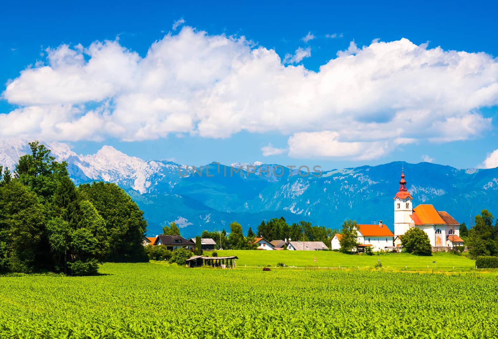 Beautiful Alpine village in Slovenia. Mountains and cloudy sky. Green meadow and the old Church