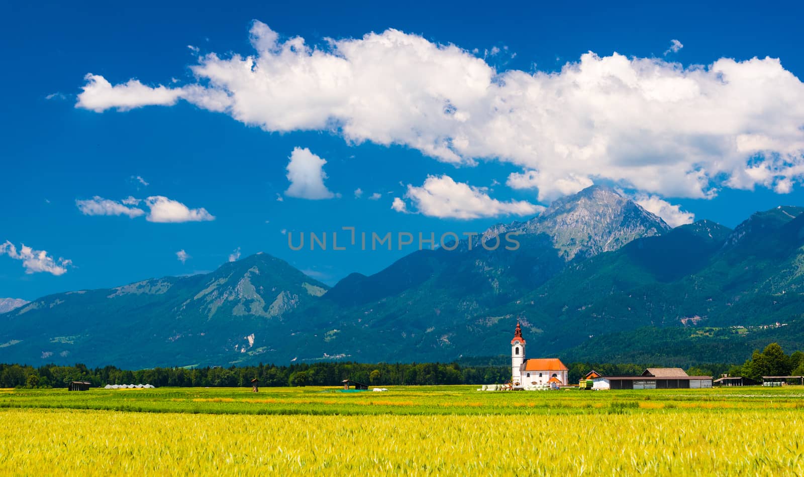 Old Church in the field. Picturesque landscape with mountains, hills and blue sky with clouds. Slovenia.