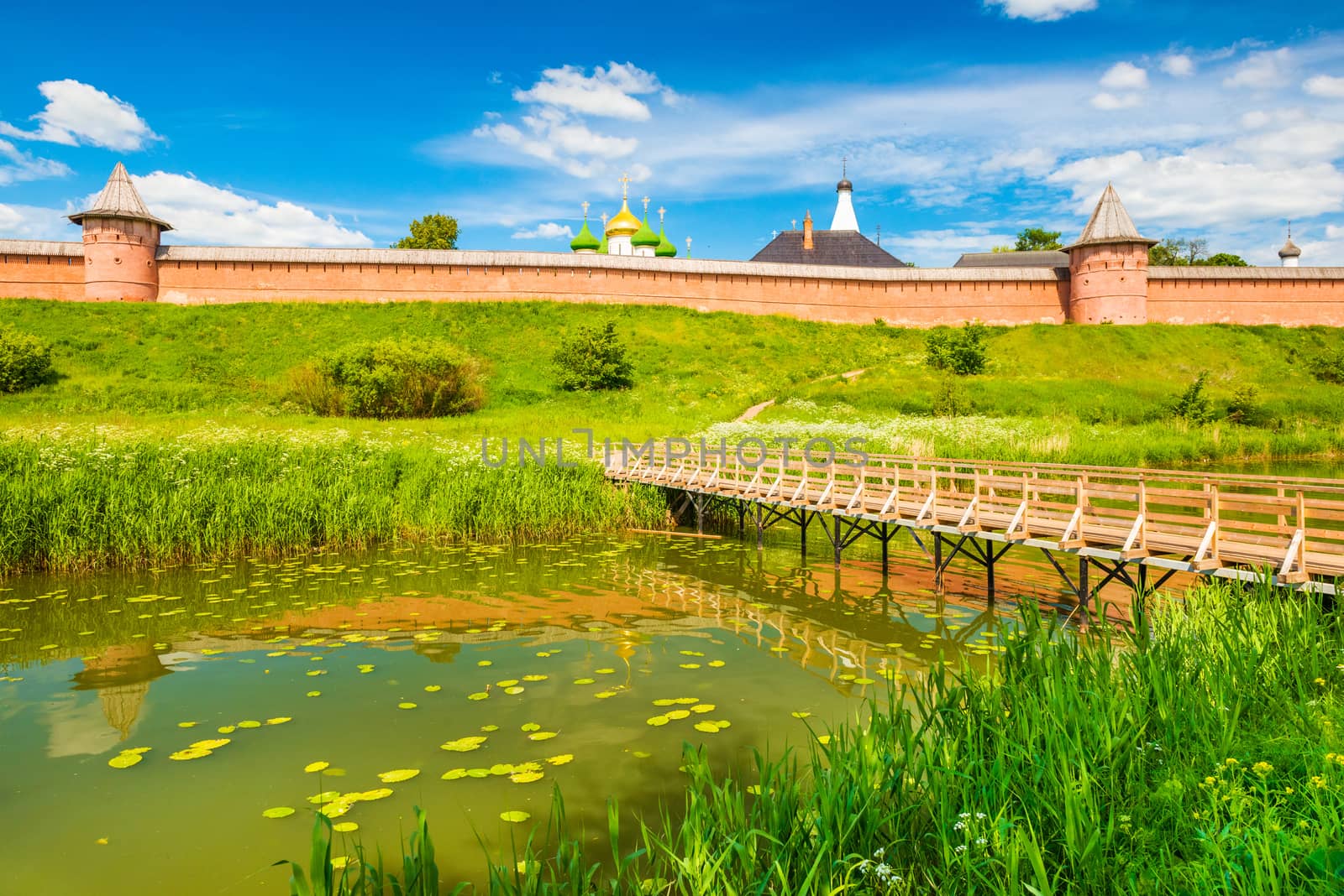 Suzdal cityscape on a summer day. Panorama of the old Russian historic town with traditional architecture and wooden bridge across the river. The Golden Ring of Russia.
