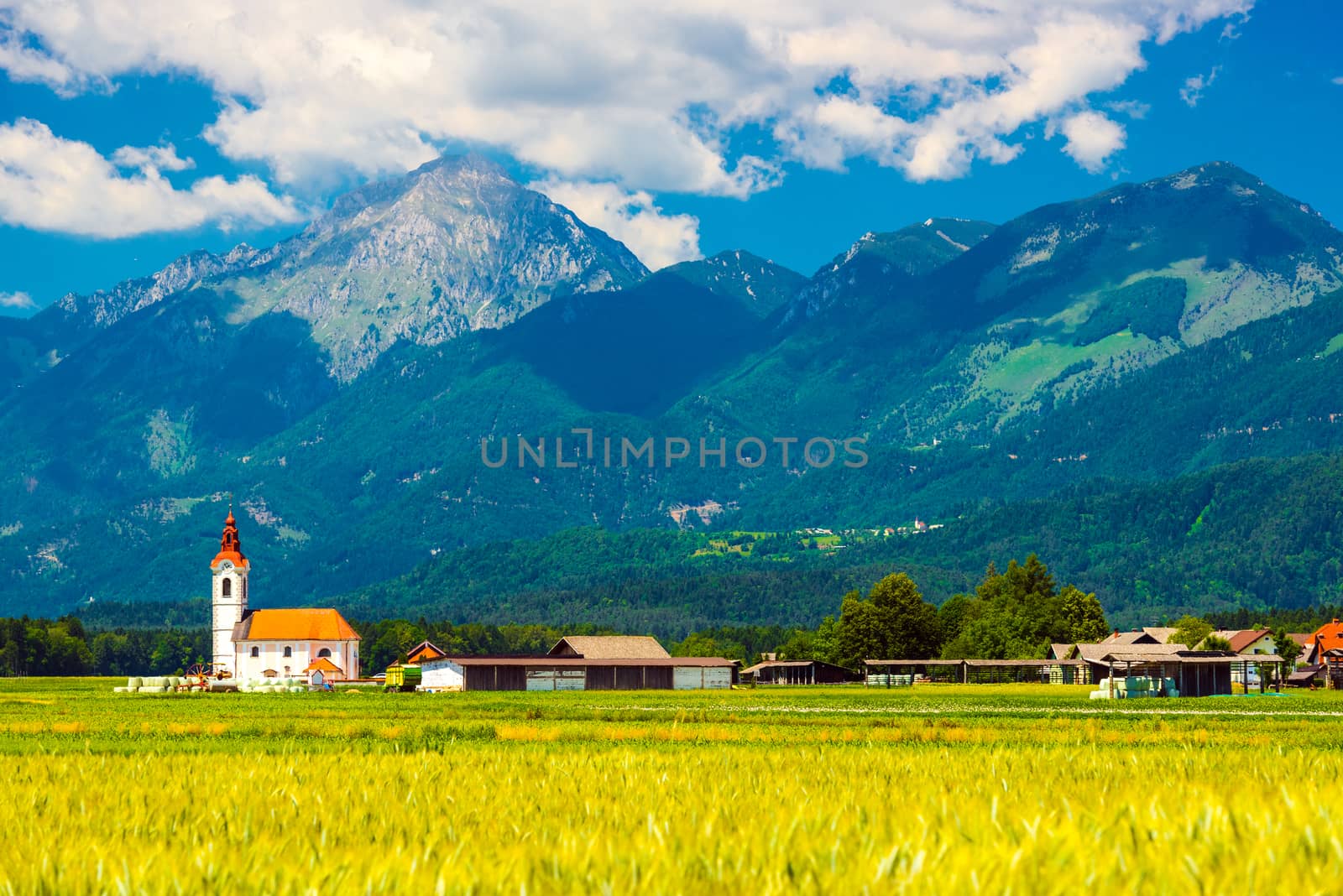 Beautiful summer landscape of a small village with an old chapel in Slovenia. Picturesque mountain range with green hills and forest. Wide angle panorama, mountains against the blue sky with clouds.