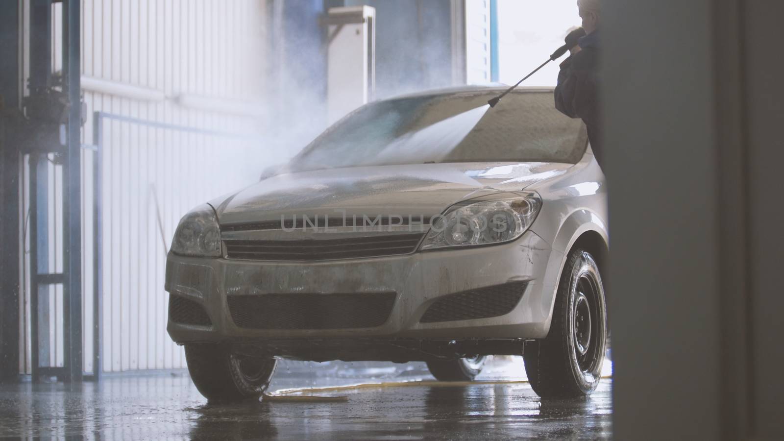 Woman worker with the water hose in car-washing facility, telephoto shot