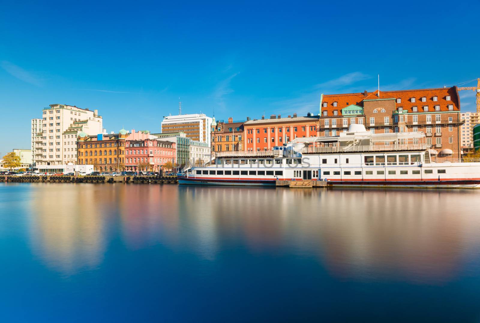 Skyline of a city reflected in water. Cityscape of Malmo with historic and modern architecture, embankment and ship, long exposure photo. Oresund region, Sweden