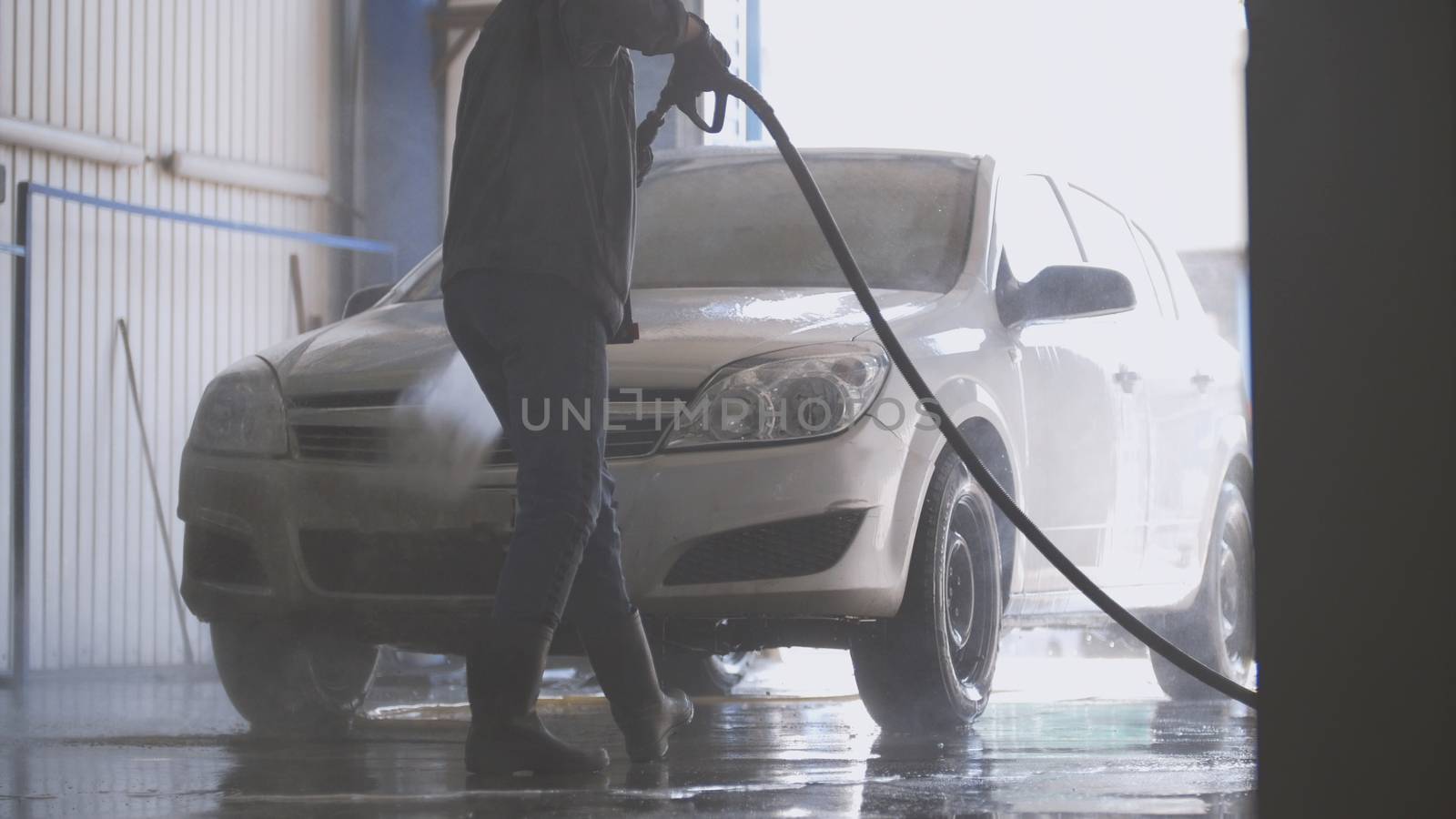 Woman worker with the water hose in car-washing facility, telephoto shot