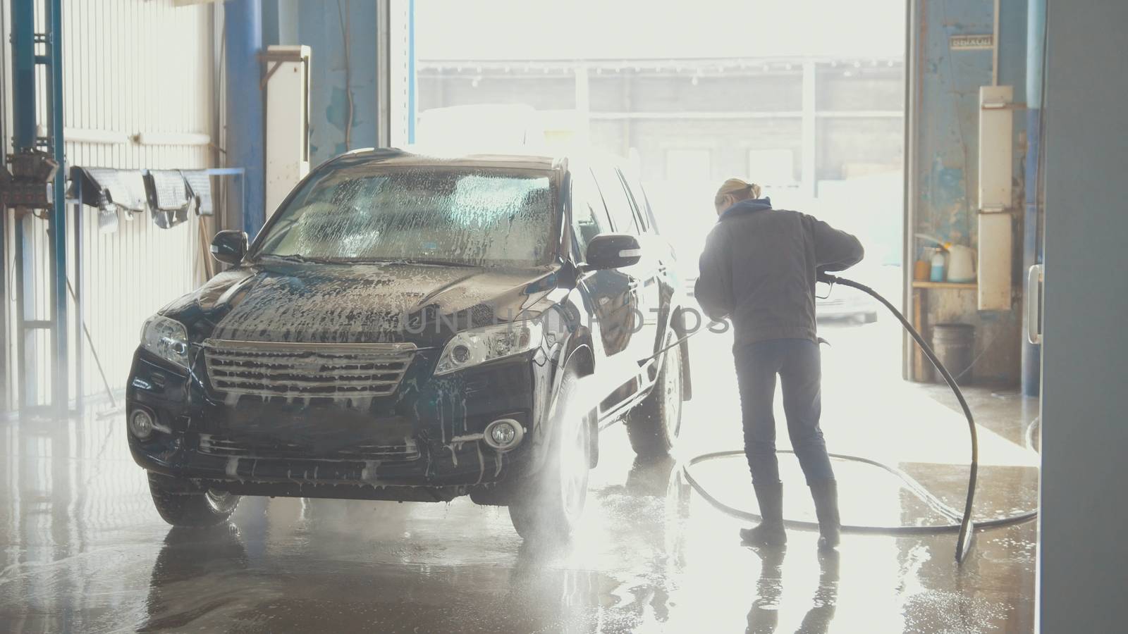Woman worker with the water hose in car-washing facility, telephoto shot