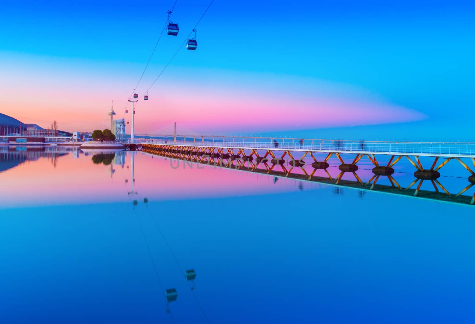 Picturesque sunset over The Park of the Nations in Lisbon, Portugal. Evening cityscape with cable car road and bridge reflected in the water