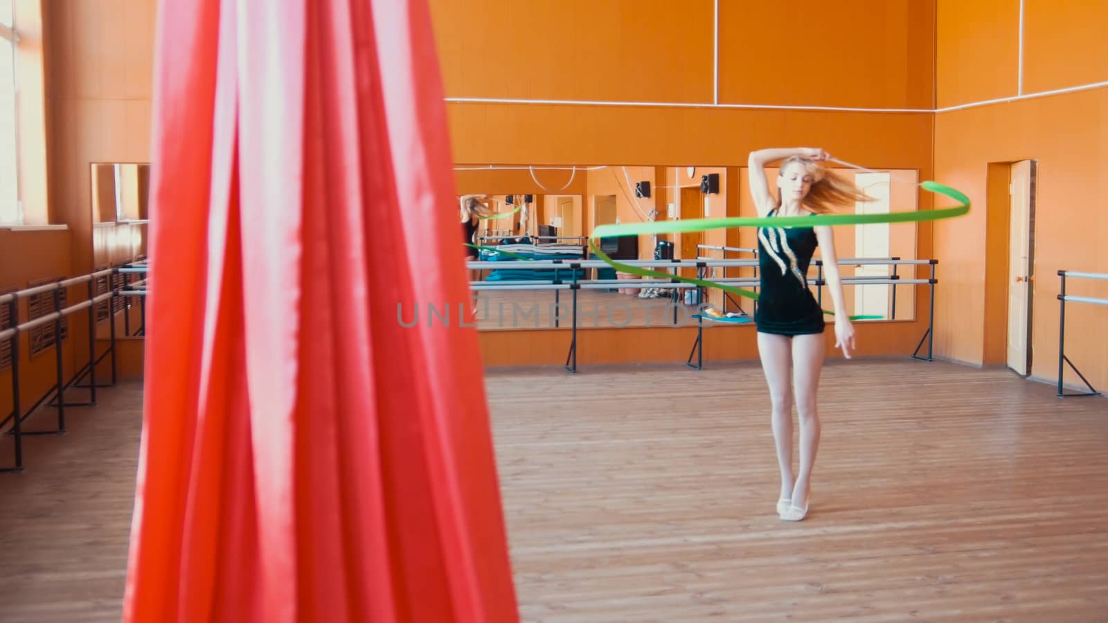 Rhythmic gymnastics - young woman training a gymnastics exercise with a green ribbon by Studia72