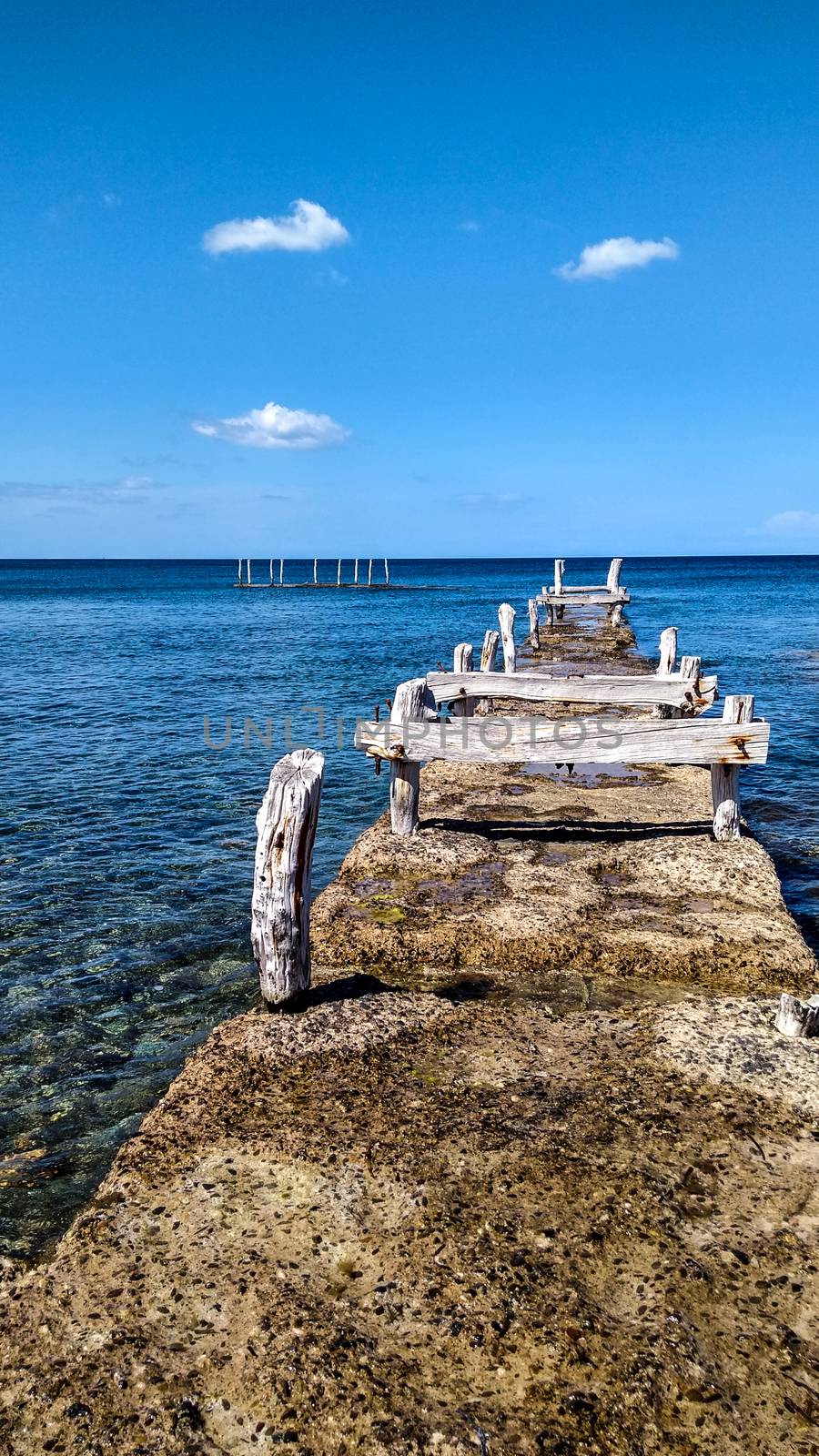 Ancient disused pier with wooden structures corroded by the atmospheric events that made it white on the crystal clear blue sea by robbyfontanesi